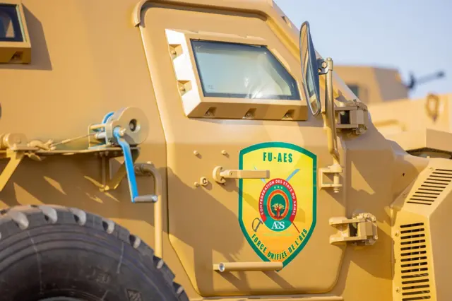 Un véhicule militaire de couleur jaune sur lequel on voit une affiche portant l'indication "FU- AES".
