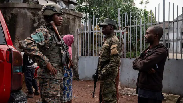 Deux militaires armés accompagnés d'un civil et d'une femme en arrière-plan dans une zone de conflit